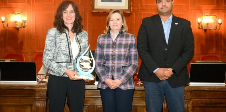 Fotografía en la que se ven tres personas, dos mujeres y un hombre, todos de mediana edad. Visten ropa formal y se encuentran en un despacho de madera con el retrato del Rey al fondo.